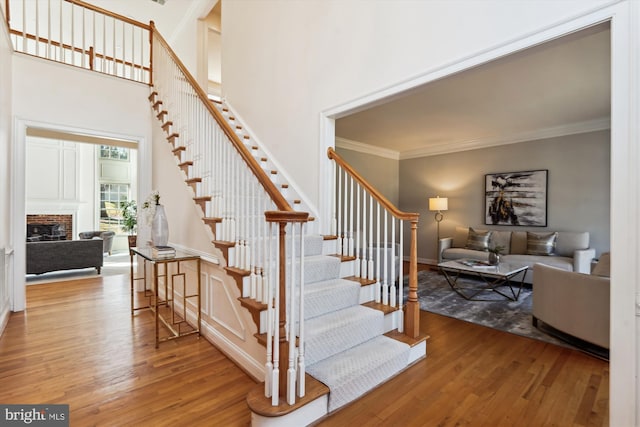 stairway featuring a brick fireplace, wood finished floors, and crown molding