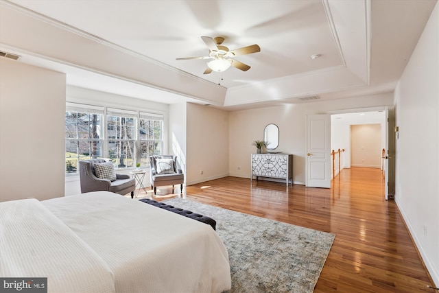 bedroom with visible vents, a raised ceiling, baseboards, and wood finished floors