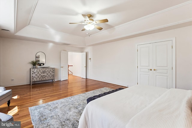 bedroom with a ceiling fan, wood finished floors, baseboards, visible vents, and a raised ceiling