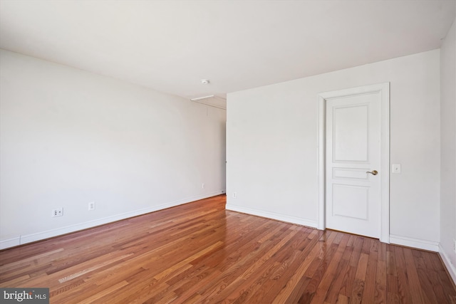 spare room with attic access, baseboards, and wood finished floors