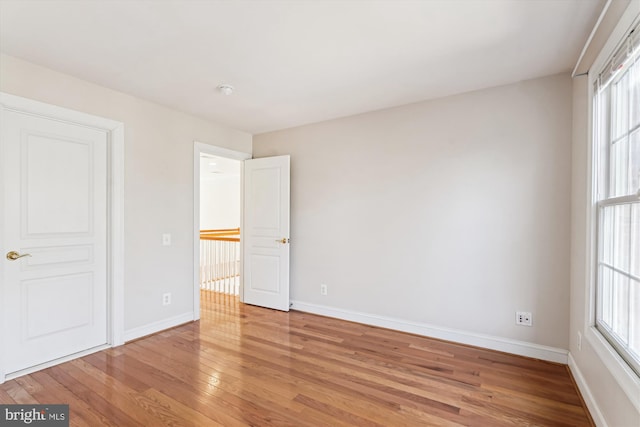 unfurnished bedroom featuring multiple windows, light wood-style flooring, and baseboards