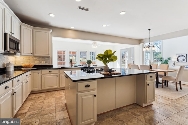 kitchen featuring dark countertops, stainless steel microwave, visible vents, decorative backsplash, and gas cooktop