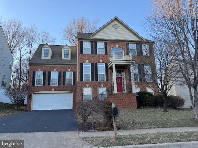 colonial-style house with aphalt driveway, brick siding, a balcony, and an attached garage