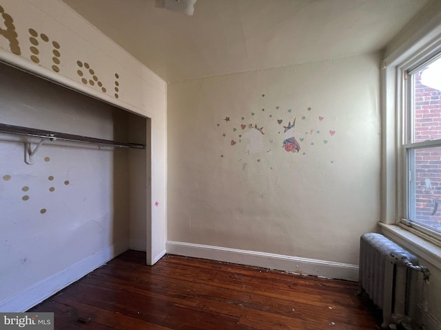 unfurnished bedroom with a closet, radiator, baseboards, and wood-type flooring