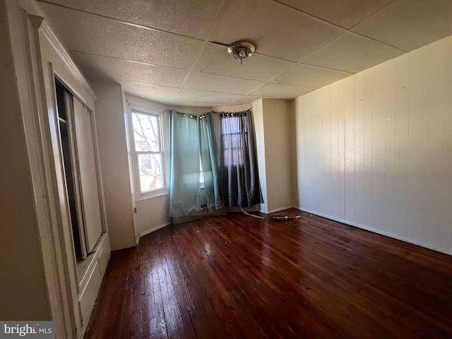 unfurnished room with a drop ceiling, baseboards, and hardwood / wood-style flooring