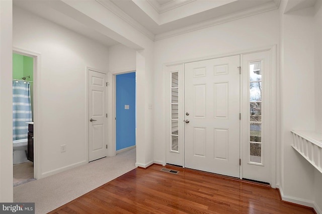 foyer entrance with visible vents, wood finished floors, baseboards, and ornamental molding