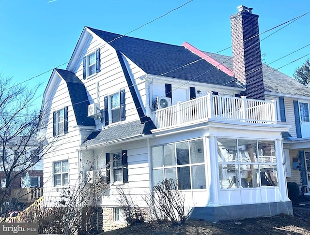 view of property exterior with a balcony, roof with shingles, a gambrel roof, a sunroom, and a chimney