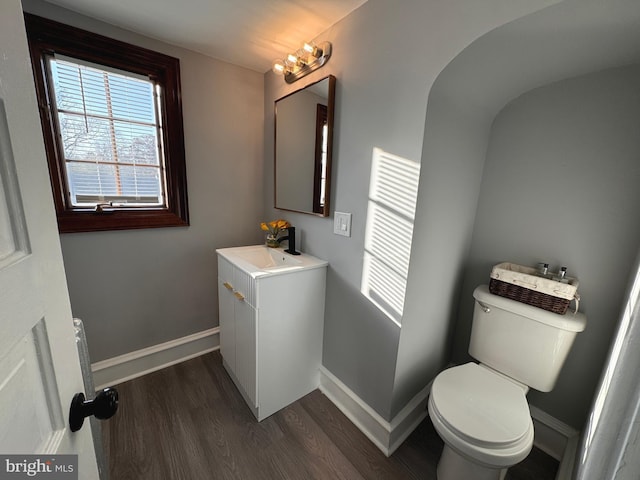 half bath with baseboards, toilet, wood finished floors, and vanity