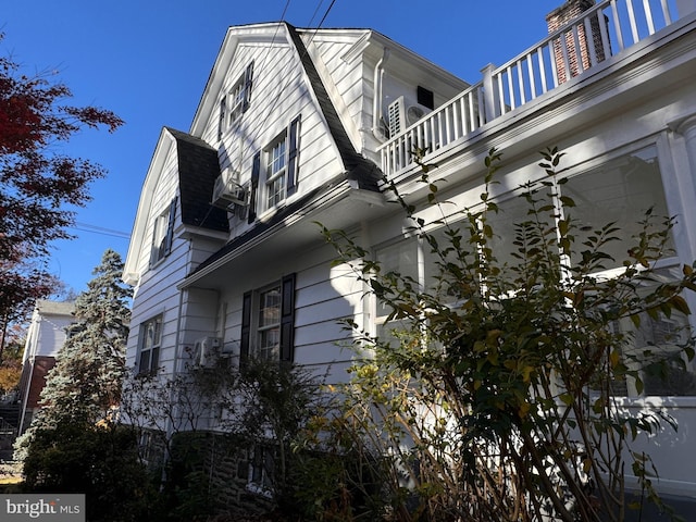 view of property exterior featuring a balcony and a gambrel roof