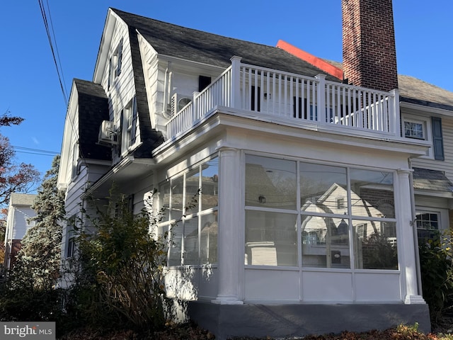 view of property exterior featuring a gambrel roof, a chimney, roof with shingles, and a sunroom