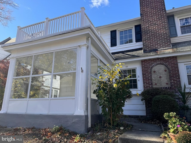 exterior space featuring a balcony, brick siding, and a sunroom