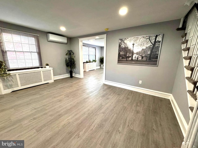 spare room with a wall unit AC, radiator, wood finished floors, and baseboards