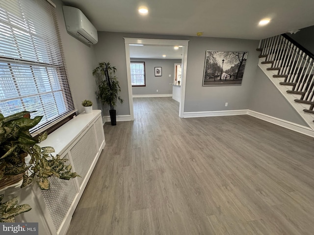 unfurnished living room featuring visible vents, baseboards, an AC wall unit, stairs, and wood finished floors