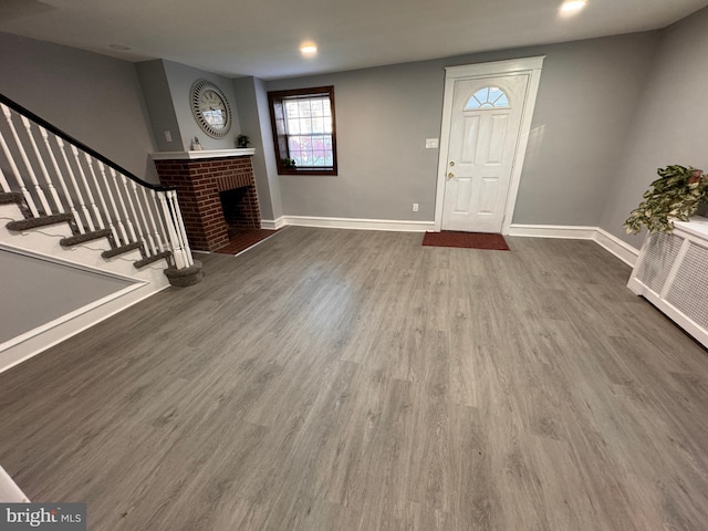 entryway with wood finished floors, recessed lighting, stairway, baseboards, and a brick fireplace