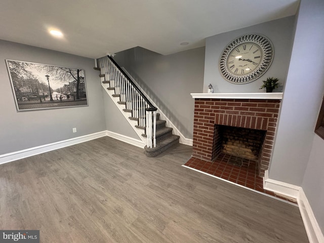 unfurnished living room with stairway, baseboards, a brick fireplace, and wood finished floors