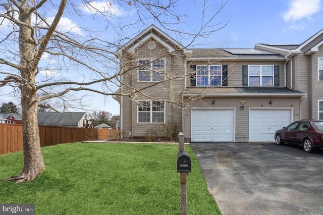 view of front of property featuring aphalt driveway, fence, a front yard, and roof mounted solar panels