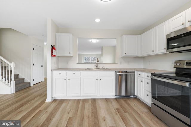 kitchen with light wood-type flooring, light countertops, white cabinets, stainless steel appliances, and a sink