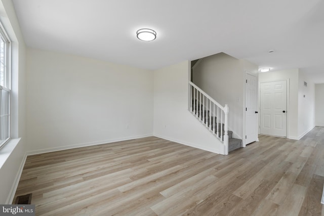 empty room featuring light wood-type flooring, stairway, baseboards, and visible vents