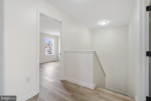 hallway featuring baseboards, an upstairs landing, and wood finished floors