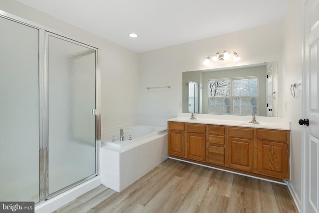 bathroom with a shower stall, double vanity, wood finished floors, a bath, and a sink