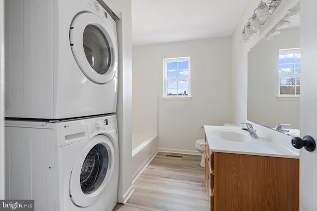 washroom with baseboards, light wood-type flooring, stacked washer and dryer, laundry area, and a sink