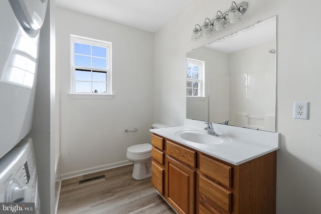 full bath with vanity, wood finished floors, visible vents, stacked washing maching and dryer, and toilet