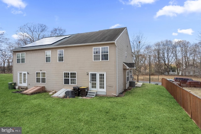 rear view of property featuring roof mounted solar panels, entry steps, a yard, and fence