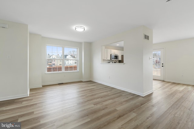 unfurnished living room with light wood-style flooring, visible vents, and a wealth of natural light