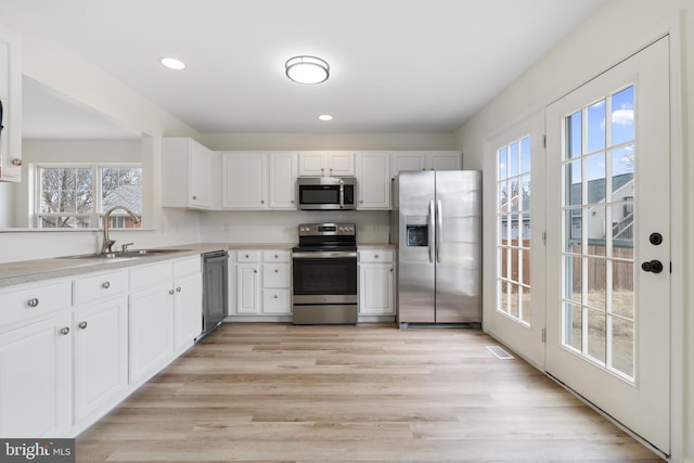 kitchen with light wood-style flooring, a sink, stainless steel appliances, white cabinets, and light countertops