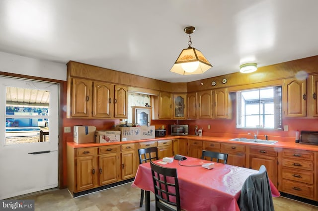 kitchen with a toaster, light countertops, brown cabinets, hanging light fixtures, and a sink