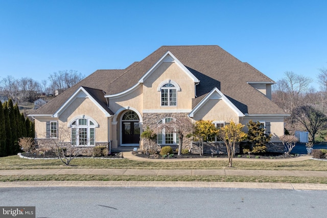 traditional-style home featuring a shingled roof, stone siding, and stucco siding