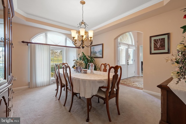 dining area with a raised ceiling, baseboards, arched walkways, and light carpet