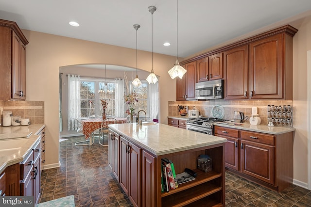 kitchen featuring baseboards, a center island with sink, a sink, decorative backsplash, and appliances with stainless steel finishes