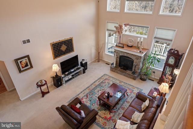 carpeted living room with visible vents, plenty of natural light, a stone fireplace, and baseboards