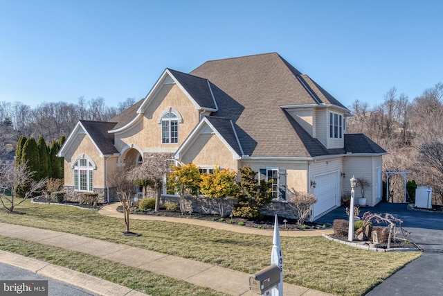 traditional-style house featuring a shingled roof, a front lawn, stone siding, and aphalt driveway