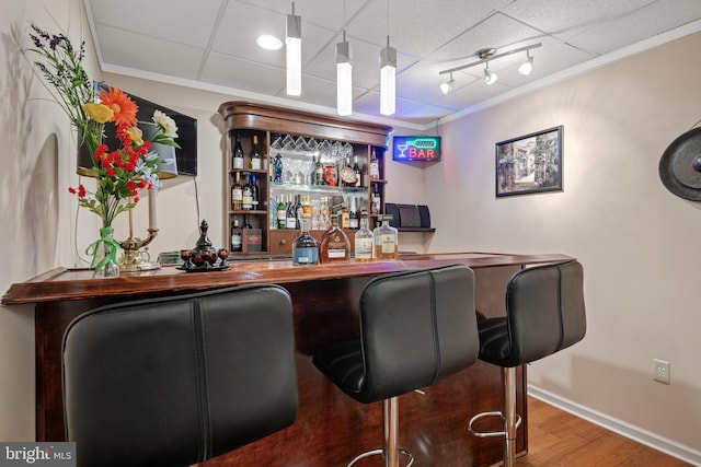 bar featuring track lighting, wood finished floors, a bar, crown molding, and baseboards