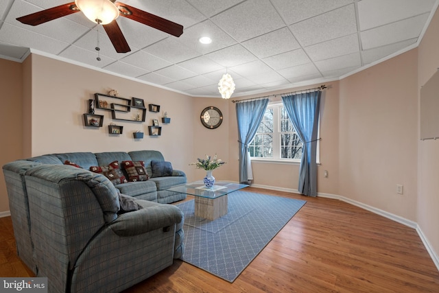 living area with a drop ceiling, baseboards, wood finished floors, and ornamental molding