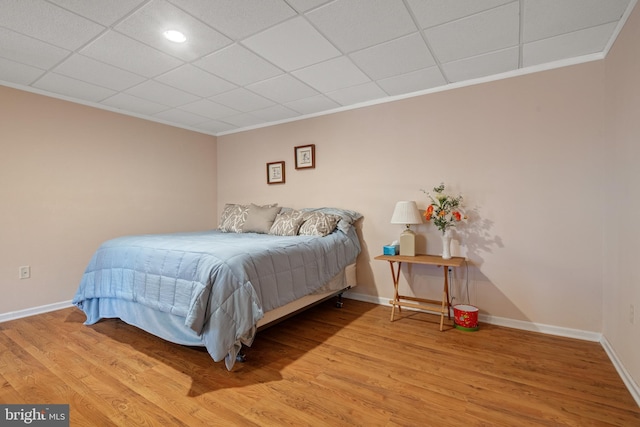 bedroom with crown molding, wood finished floors, baseboards, and a drop ceiling