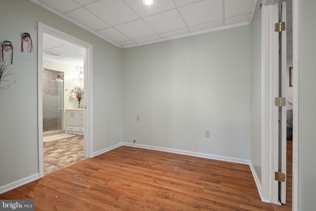 unfurnished bedroom with a drop ceiling, connected bathroom, light wood-type flooring, and baseboards