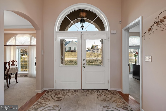 foyer entrance featuring baseboards, arched walkways, wood finished floors, and carpet flooring