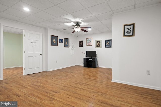 unfurnished living room featuring a drop ceiling, light wood-type flooring, baseboards, and ceiling fan