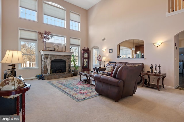 carpeted living area with visible vents, arched walkways, a high ceiling, a stone fireplace, and baseboards