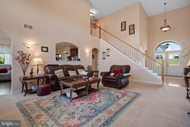 carpeted living room with arched walkways, visible vents, stairs, and baseboards