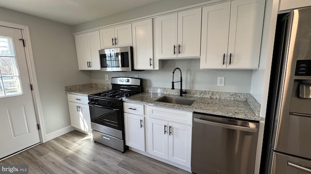 kitchen with light wood-style flooring, a sink, light stone counters, appliances with stainless steel finishes, and white cabinets