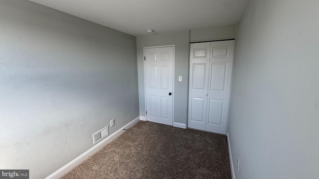 unfurnished bedroom featuring a closet, visible vents, baseboards, and dark colored carpet