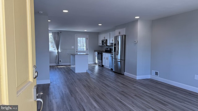 kitchen with a kitchen island, dark wood-type flooring, baseboards, stainless steel appliances, and white cabinetry