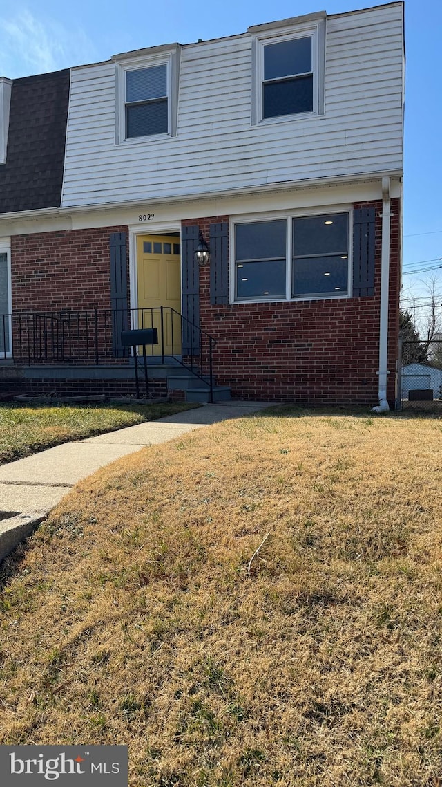 view of front of property with brick siding, mansard roof, a front yard, and roof with shingles