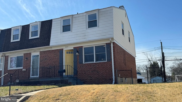 view of front facade with brick siding, a shingled roof, and a front lawn