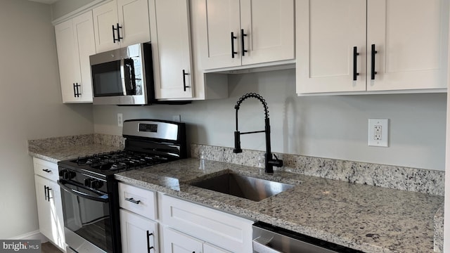 kitchen featuring light stone counters, appliances with stainless steel finishes, white cabinetry, and a sink