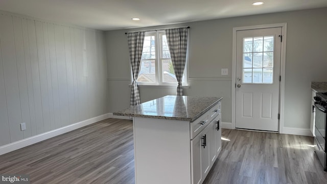 kitchen with light stone counters, white cabinets, a kitchen island, and light wood-type flooring